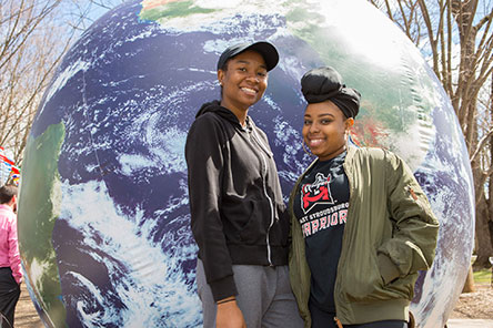 two female students standing in front of a giant global