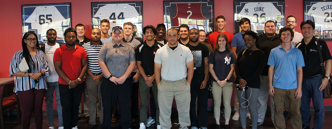 Sport Management students on a tour, standing in front of framed baseball jerseys